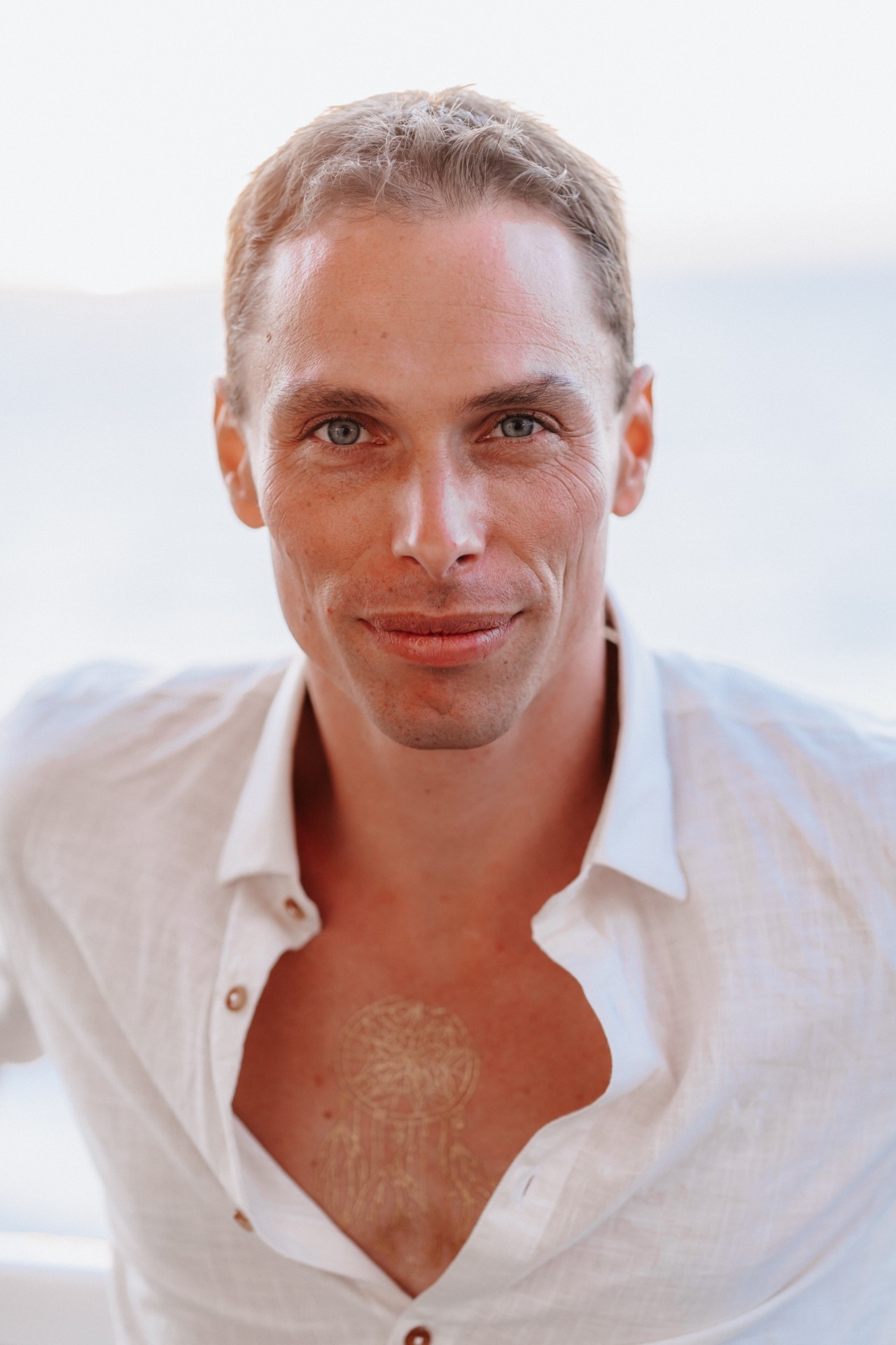Sébastien Roger smiling in warm daylight, wearing an open white linen shirt